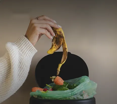 Hand gooit een bananenschil in een afvalemmer