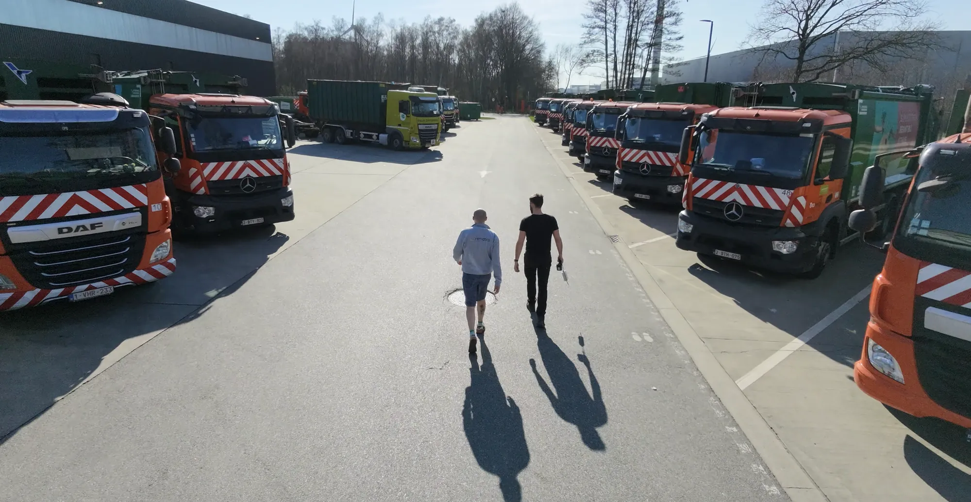 Deux collaborateurs de Rematics marchent entre une flotte de camions de collecte